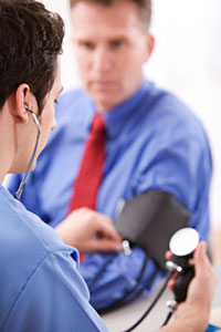 A man in a blue dress shirt and red tie is getting his blood pressure checked